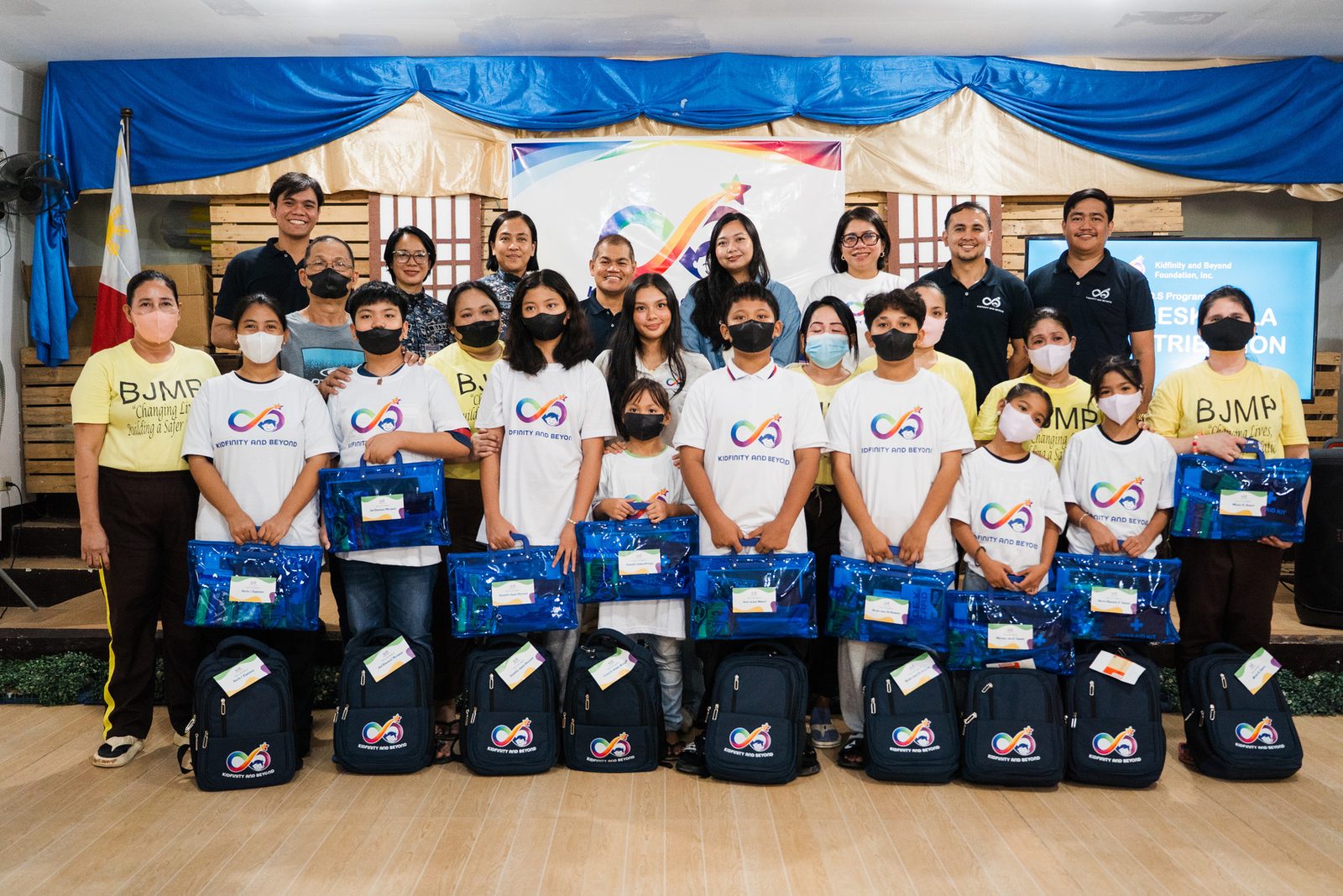 Children holding school kit bags with Kidfinity and Beyond staff