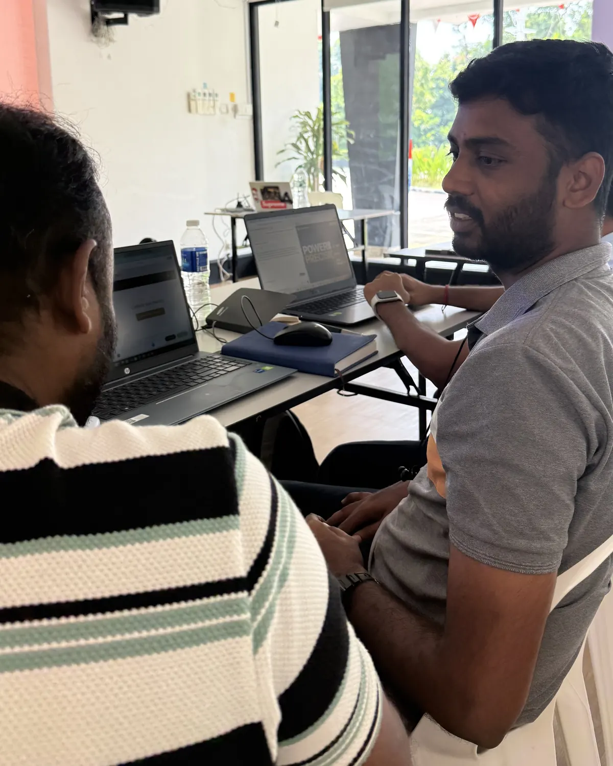 Two learners at a table in Sembawang, one watching the other work on a laptop