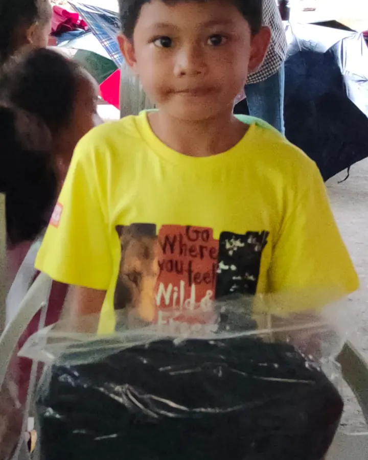 A boy in a yellow shirt holding a wrapped school bag