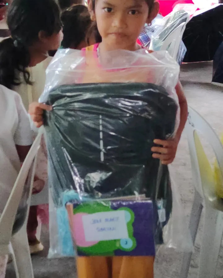 A girl holding a wrapped school bag and a notebook