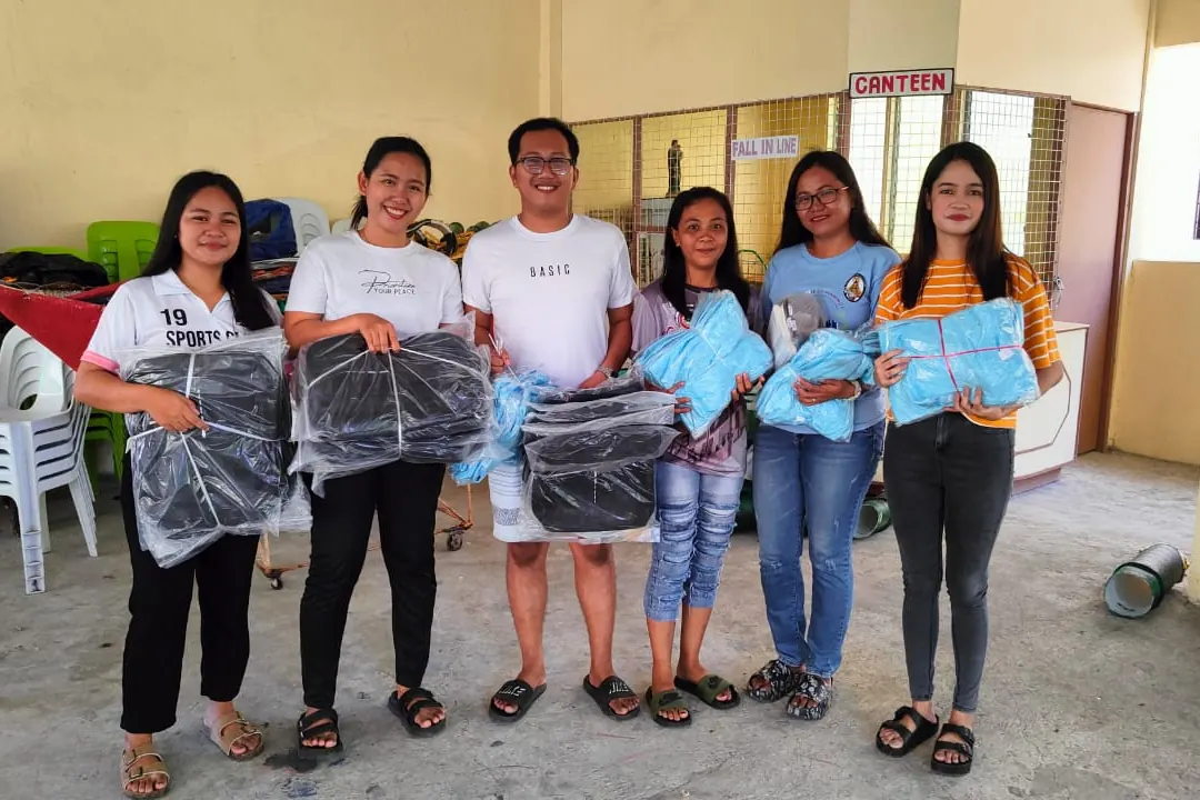 Young volunteers standing in a covered hall holding wrapped school kits