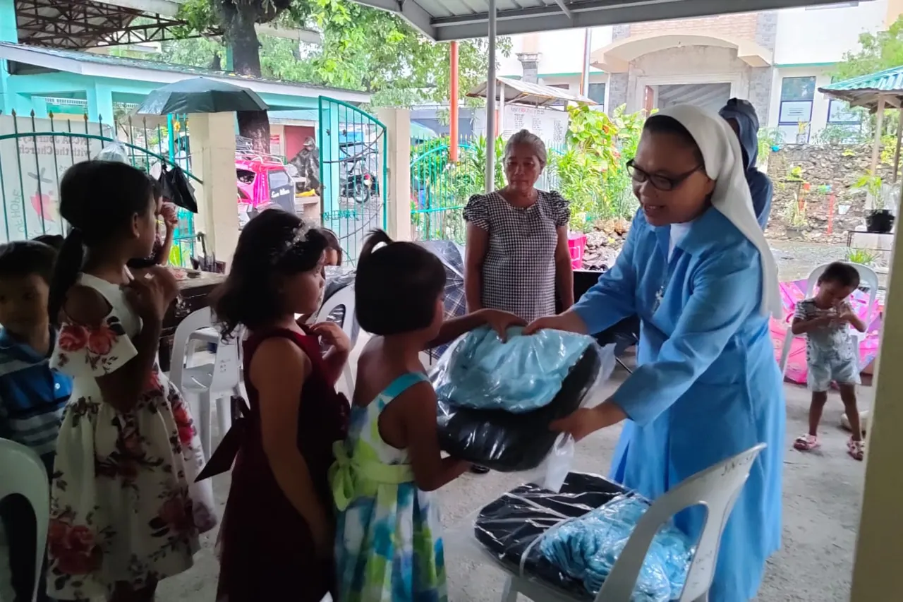 A volunteer in a blue habit hands a kit to a child