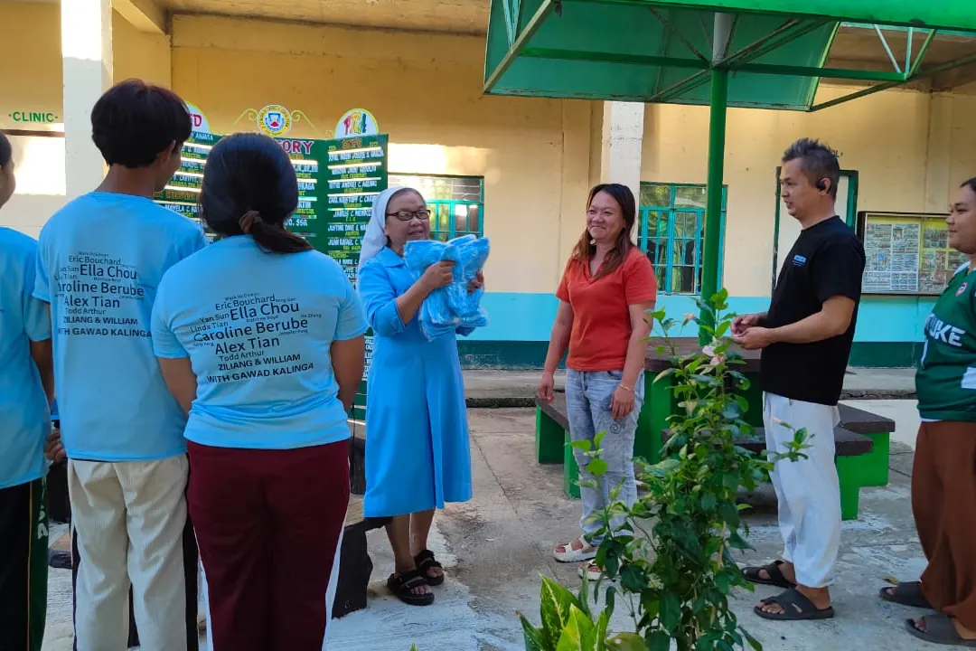Volunteers in blue printed shirts talking with staff in a schoolyard