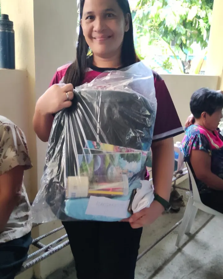 A smiling volunteer holding up a wrapped school kit