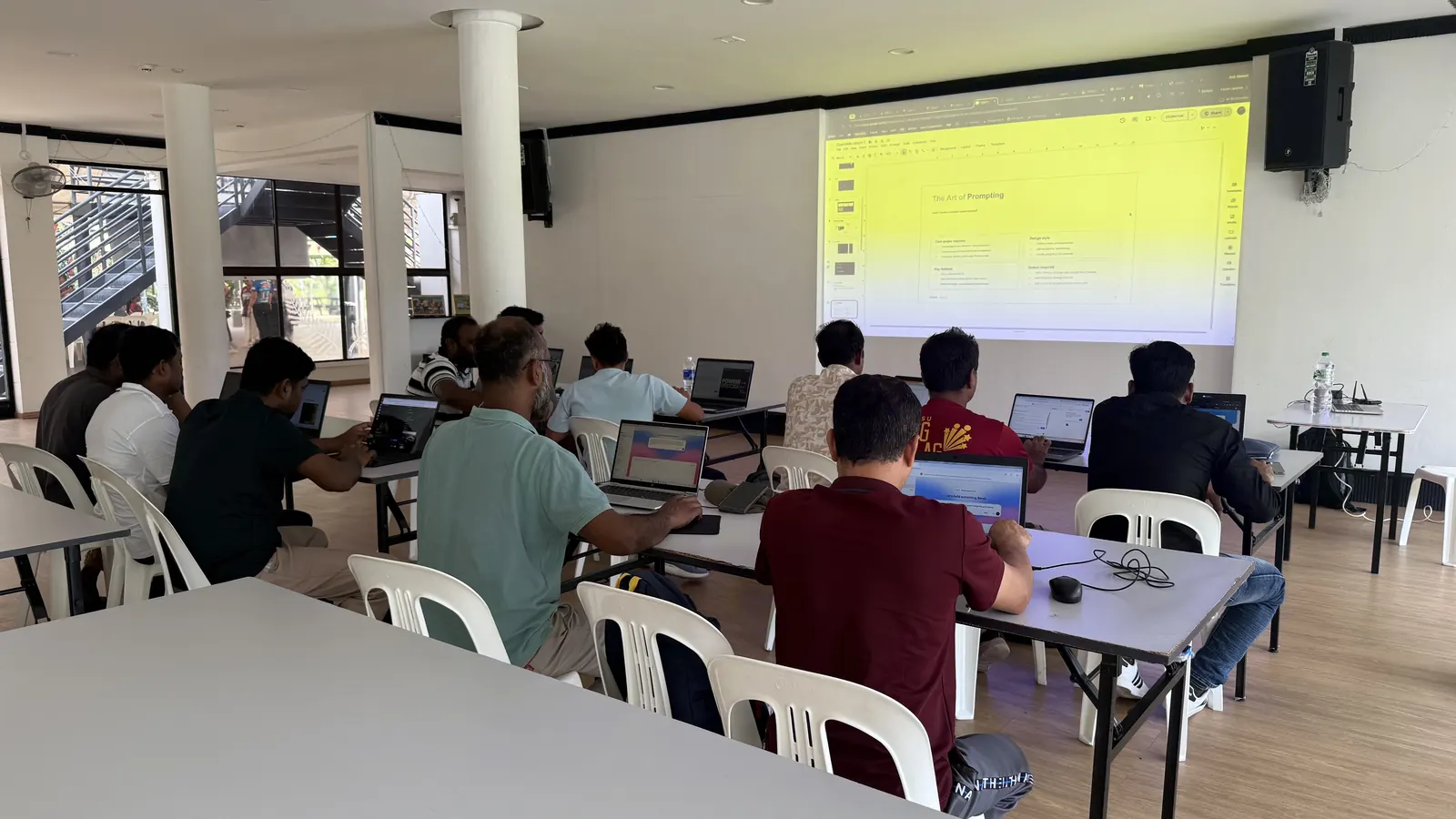Learners seated at long tables with laptops, facing a projected slide