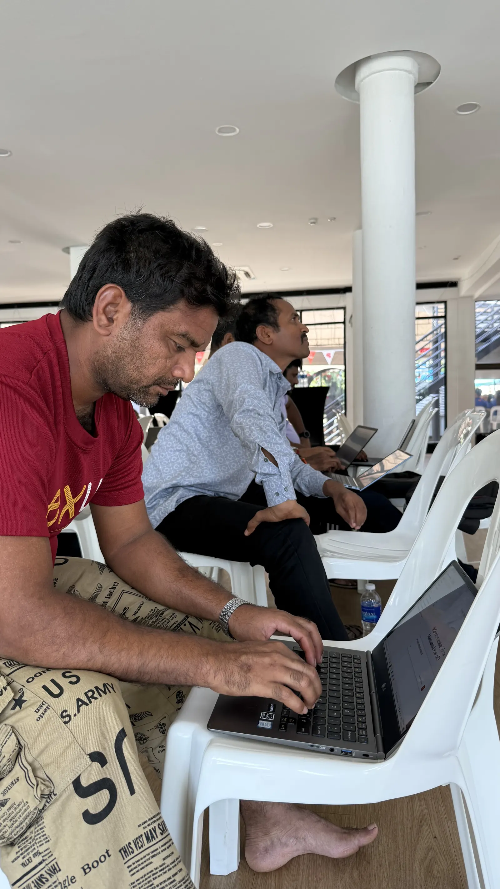A learner in a red shirt typing on a laptop on their knees