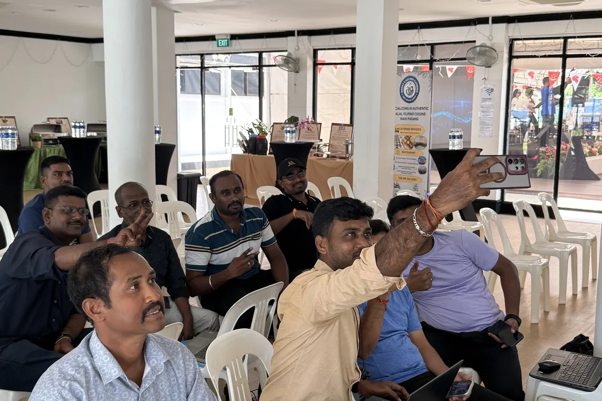A learner raises a hand with a question while others around the room look on